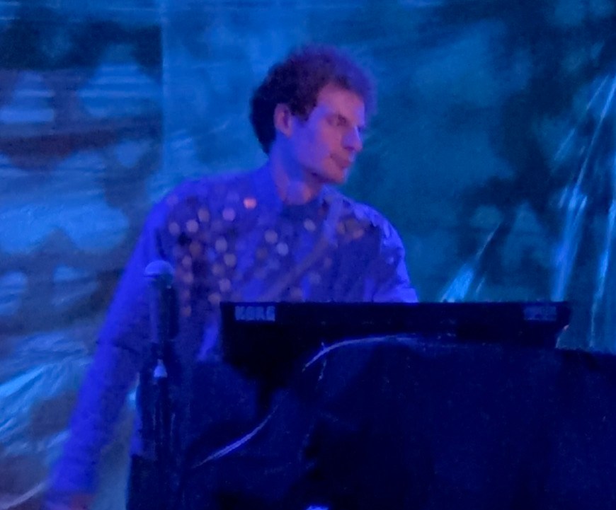 white musician with short curly hair, wearing a shiny garment